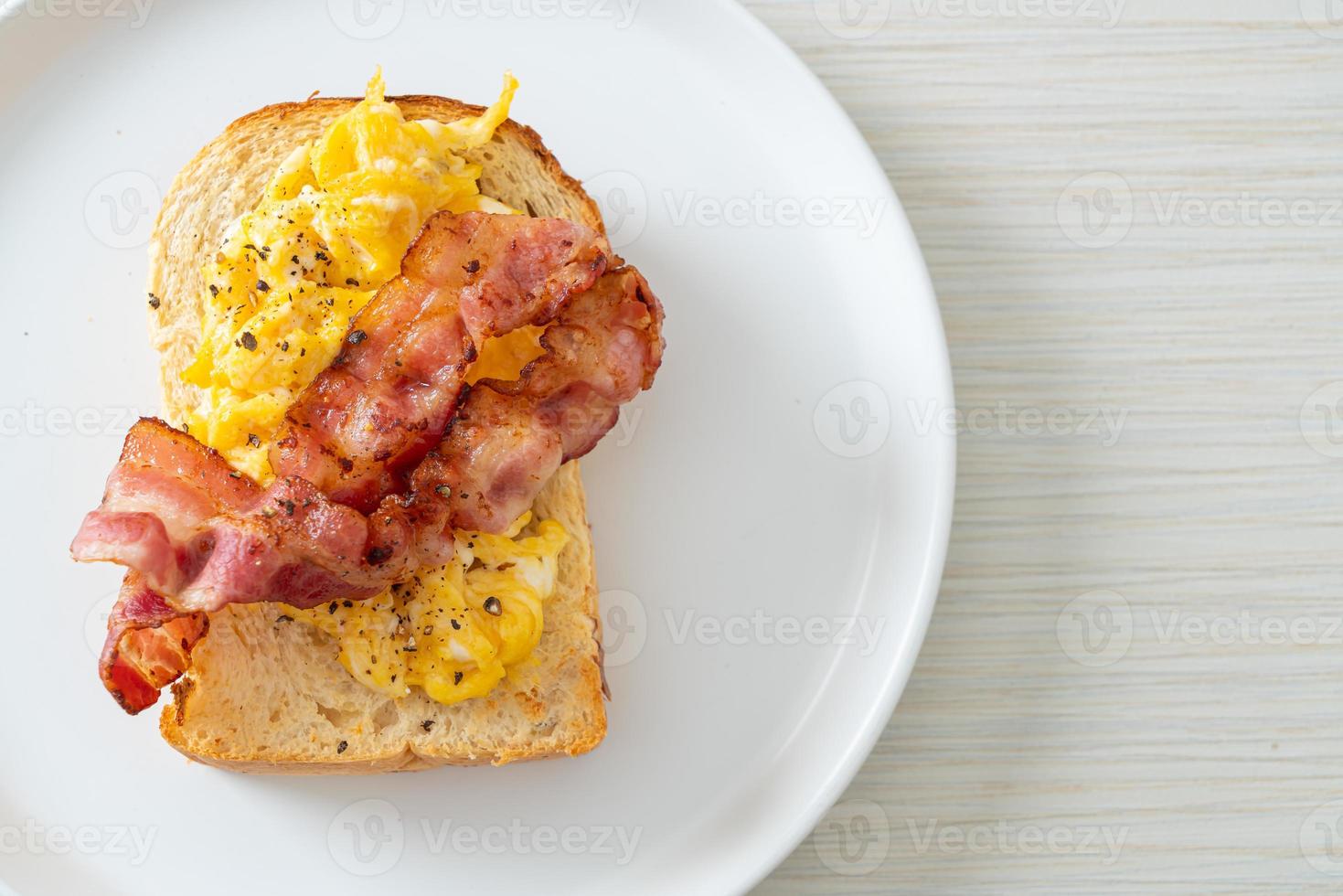 Brottoast mit Rührei und Speck auf weißem Teller foto