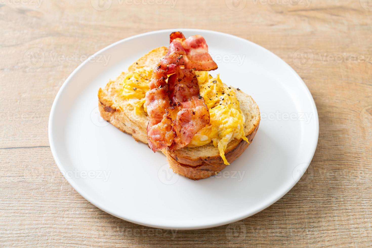 Brottoast mit Rührei und Speck auf weißem Teller foto