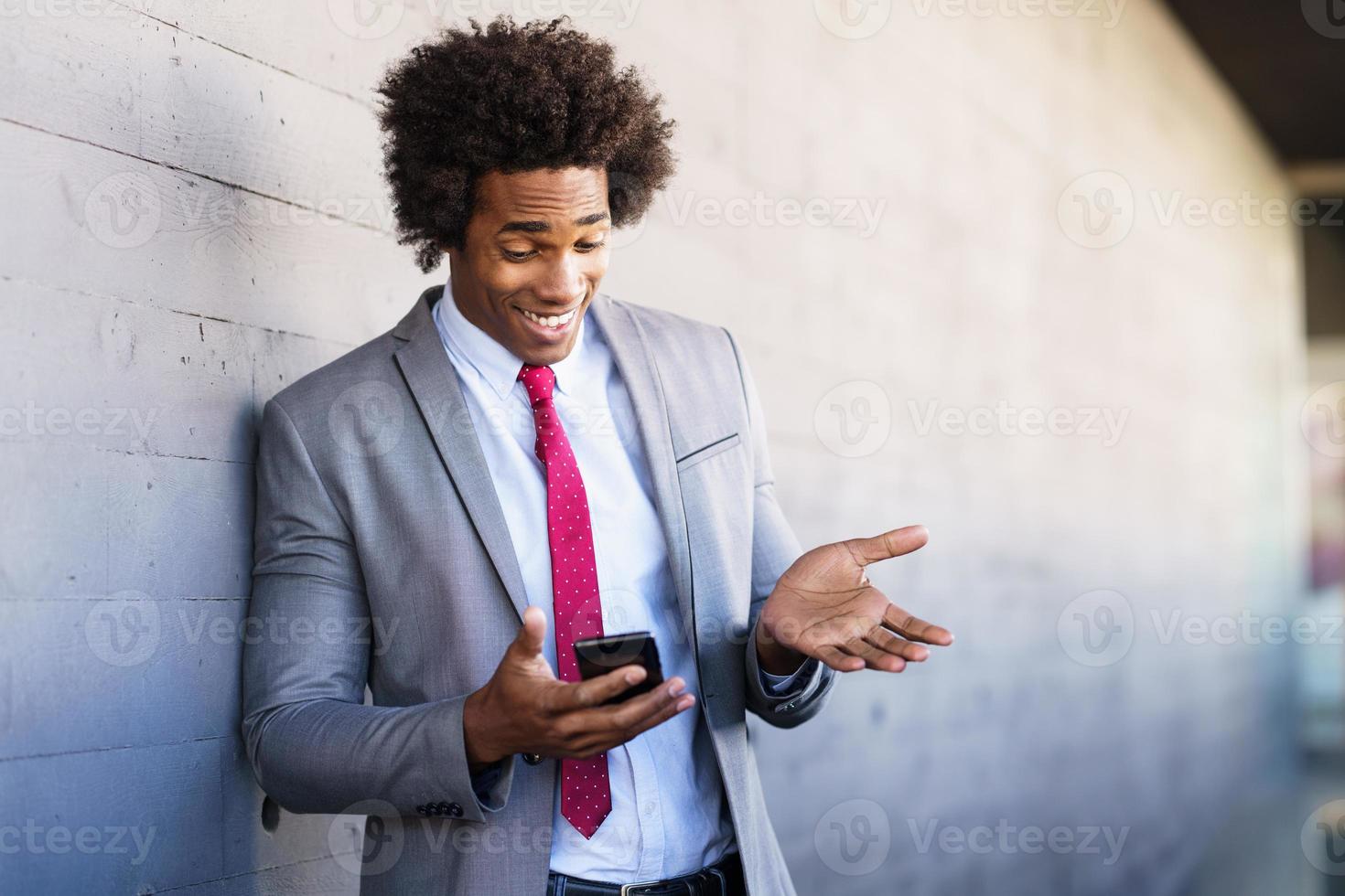 schwarzer Geschäftsmann mit einem Smartphone in der Nähe eines Bürogebäudes foto