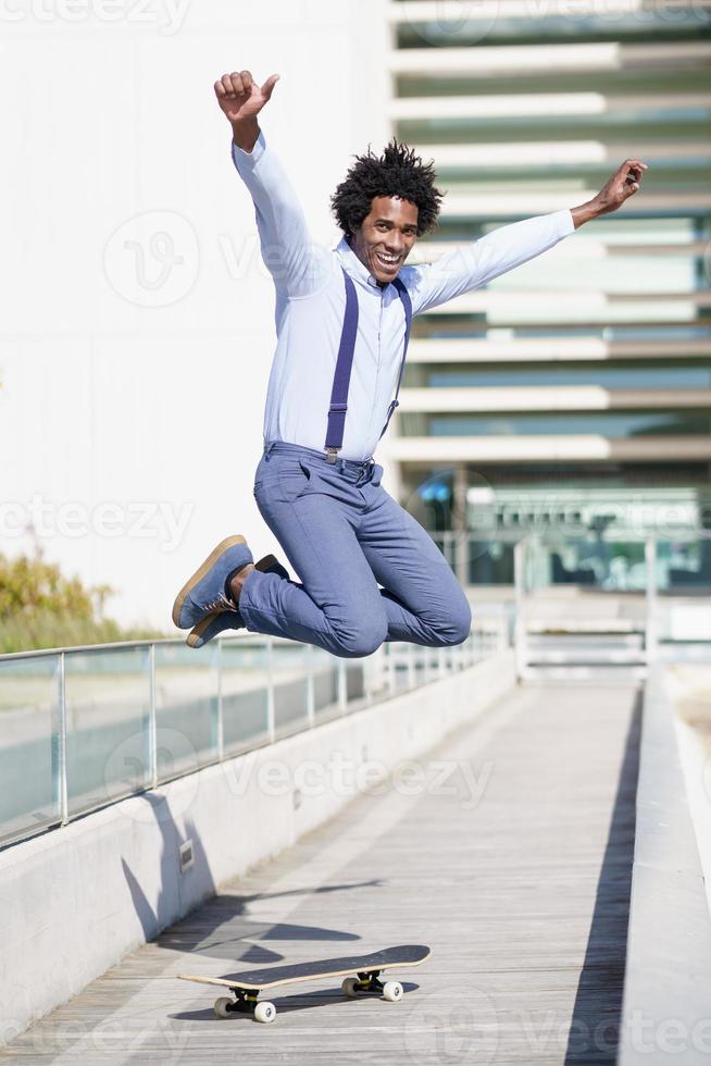 schwarzer Geschäftsmann springen auf einem Skateboard in der Nähe eines Bürogebäudes. foto