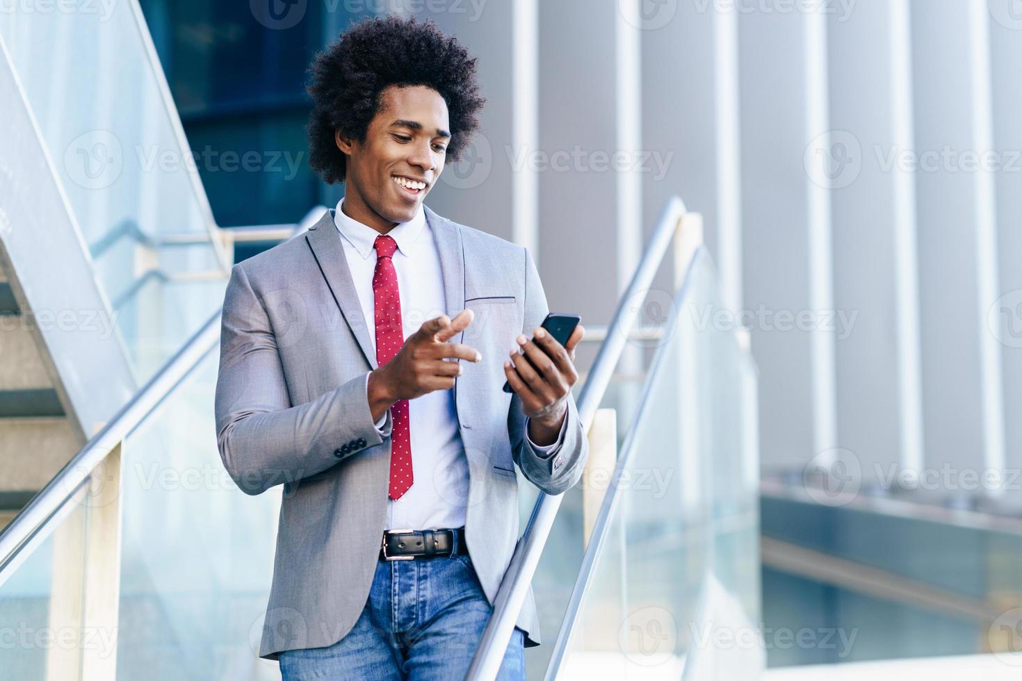 schwarzer Geschäftsmann mit einem Smartphone in der Nähe eines Bürogebäudes foto