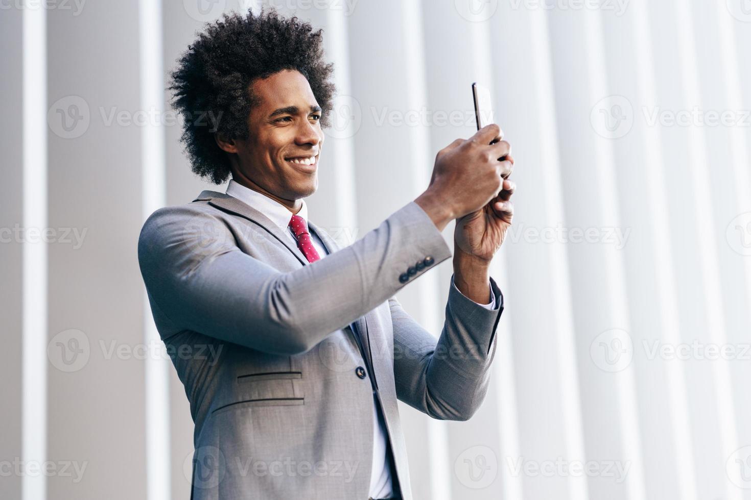 schwarzer Geschäftsmann mit einem Smartphone in der Nähe eines Bürogebäudes foto