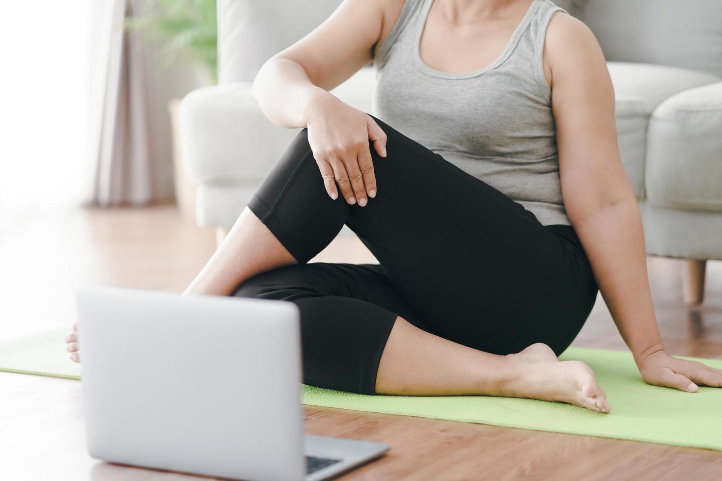 Reife asiatische mollige dicke Frau, die auf dem Boden im Wohnzimmer sitzt, praktiziert Online-Yoga-Lektion mit dem Computer. Frau mit Meditationskurs auf dem Laptop. foto