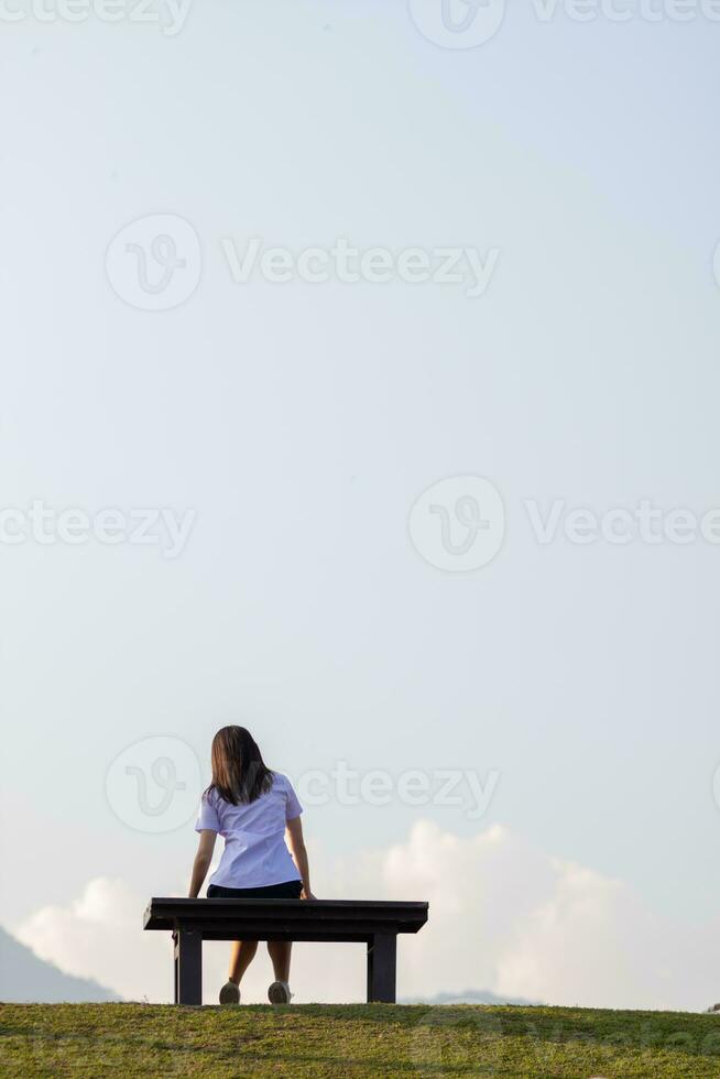 zurück Aussicht von jung Frau Sitzung auf lange Bank allein im Abend suchen beim schön Sommer- Landschaft Hintergrund von Natur und mit Kopieren Raum zum Text. Konzept Einsamkeit von Frau Wer ist allein foto