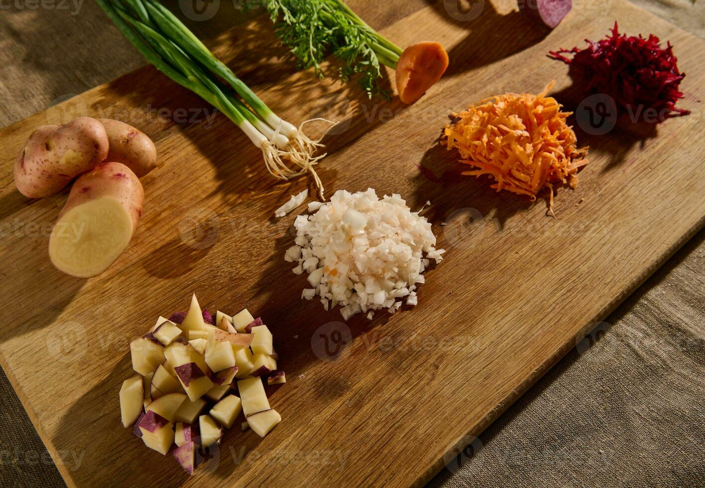 geschreddert Rübe, gerieben Karotte, Zwiebel und Würfel von Schnitt Kartoffel auf ein hölzern Tafel mit Hälften von Gemüse mit Grün Blätter und Wurzeln auf das Hintergrund. Nahansicht foto