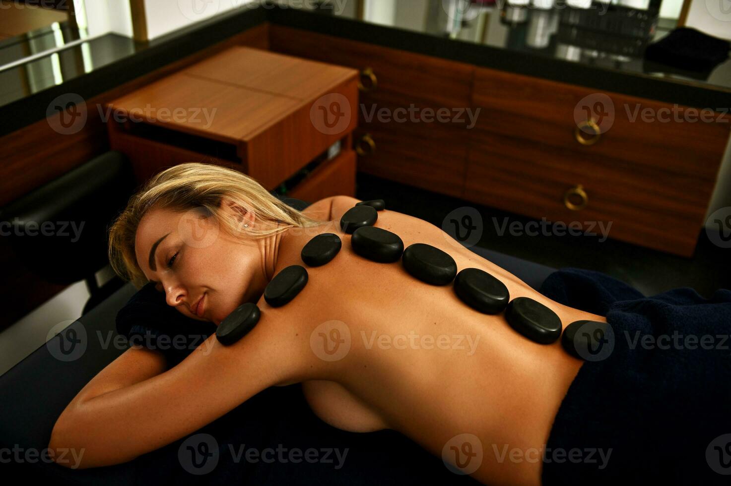 nackt Frau mit heiß Lava Steine entlang ihr Rücken Lügen auf ein Massage Tabelle beim entspannend während ayurvedisch heiß Stein Körper Behandlung foto