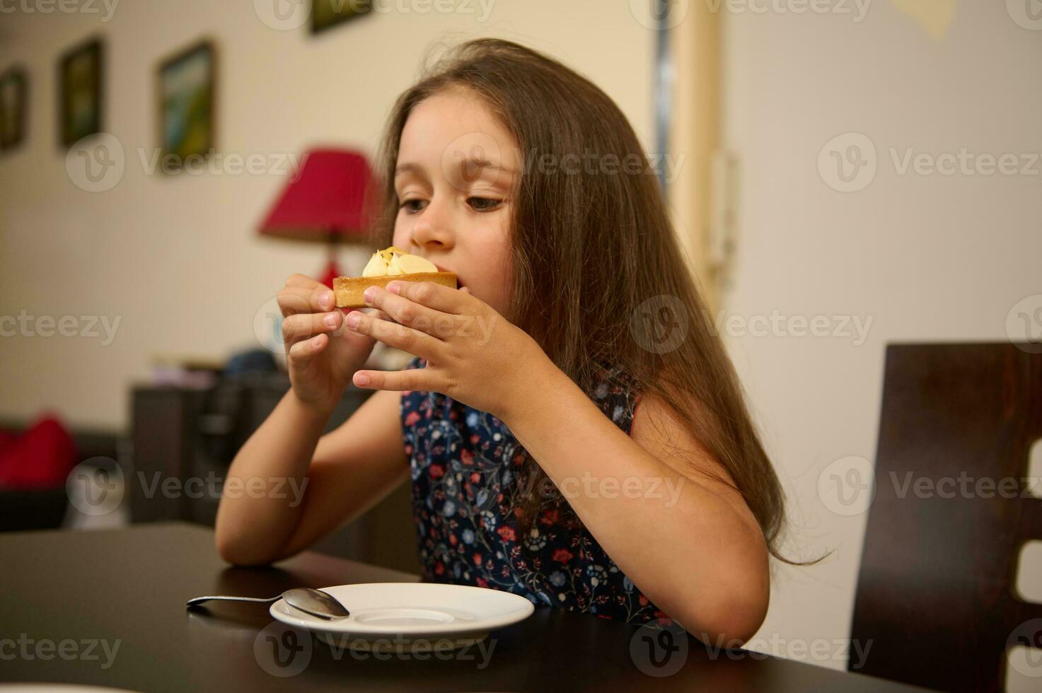schön Kind genießen ein köstlich Französisch Nachtisch, Essen mit ein Zitrone Torte, Sitzung beim Tabelle im das Leben Zimmer foto