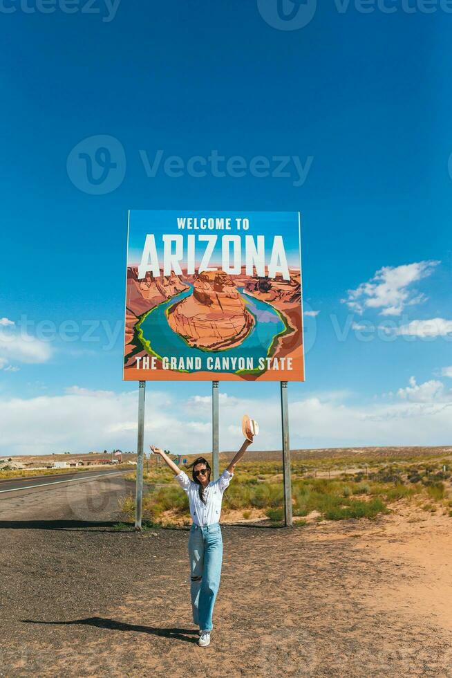 schön Frau auf ihr Ausflug zu das USA auf das Hintergrund von herzlich willkommen zu Arizona Zustand Rand Zeichen richtig im das paje Schlucht, USA foto