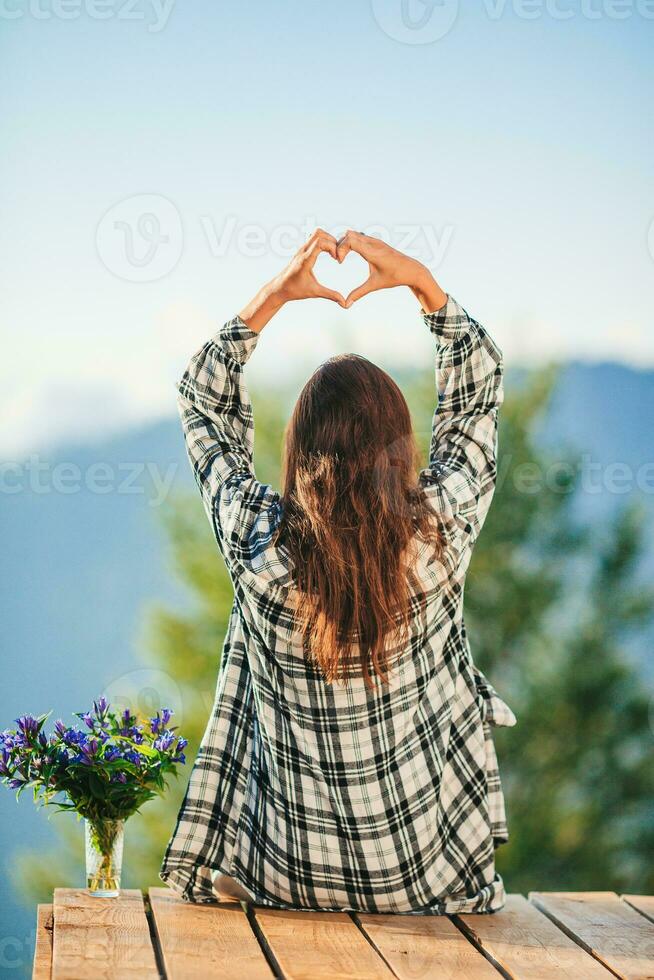 zurück Aussicht von jung Frau sitzen auf ein Terrasse beim ein Höhe im das Berge gegen das Hintergrund von Nebel und Berge foto