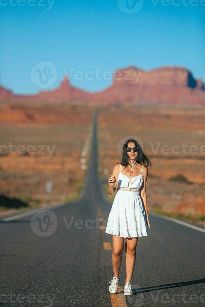 glücklich jung Frau im Weiß Kleid auf das berühmt Straße zu Monument Senke im Utah. tolle Aussicht von das Monument Schlucht. foto