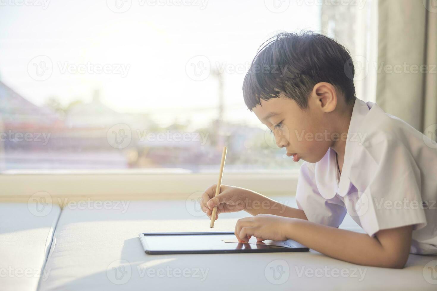 glücklich asiatisch Junge 6-7 Jahre alt, schwarz Haar, Weiß Haut, tragen Weiß Hemd und Blau kurze Hose Schreiben auf ein Tafel. Kinder im Schule Uniformen von Thailand. Konzept Über Ausbildung, spielen, Kreativität. foto