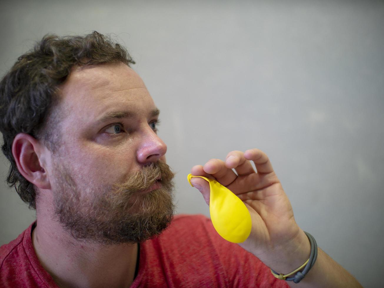 Mann mit Bart und Schnurrbart bereitet sich darauf vor, einen gelben Ballon aufzublasen foto