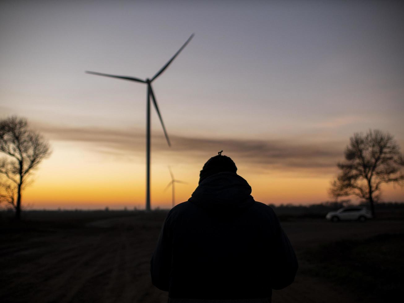 Silhouette eines Mannes bei Sonnenuntergang, der ein Foto von Windkraftanlagen macht