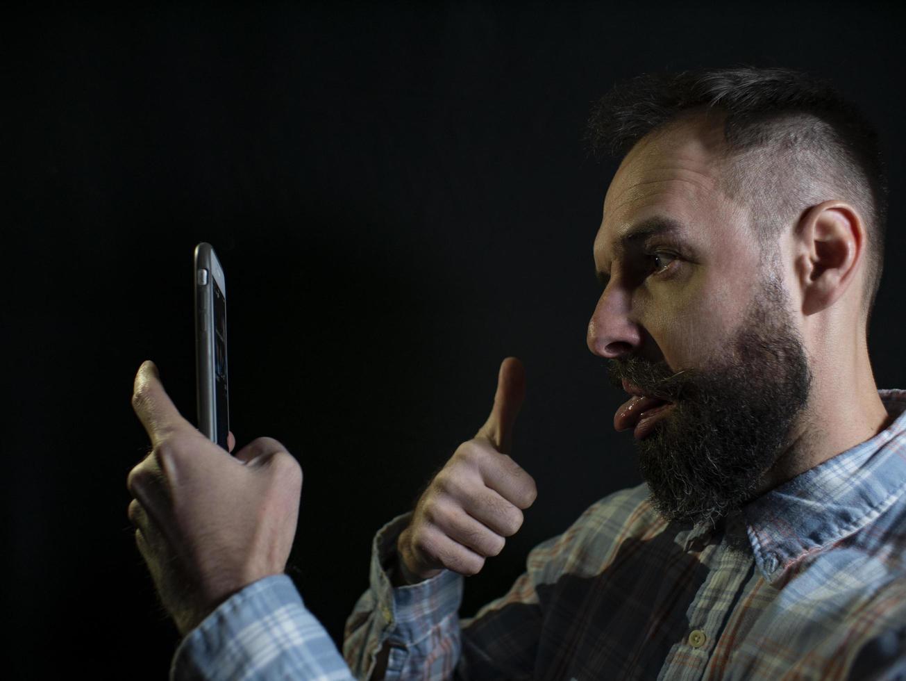 Modischer Mann mit Bart verzieht das Gesicht und macht ein Selfie am Telefon foto