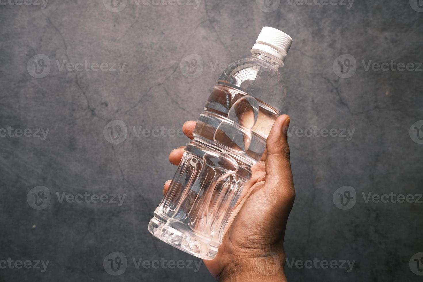 Hand, die eine frische Trinkwasserflasche vor schwarzem Hintergrund hält foto