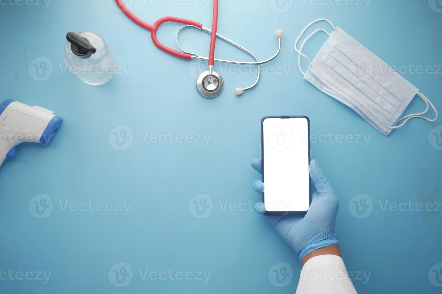 Arzthand, die Smartphone mit leerem Bildschirm auf Klinikschreibtisch hält foto