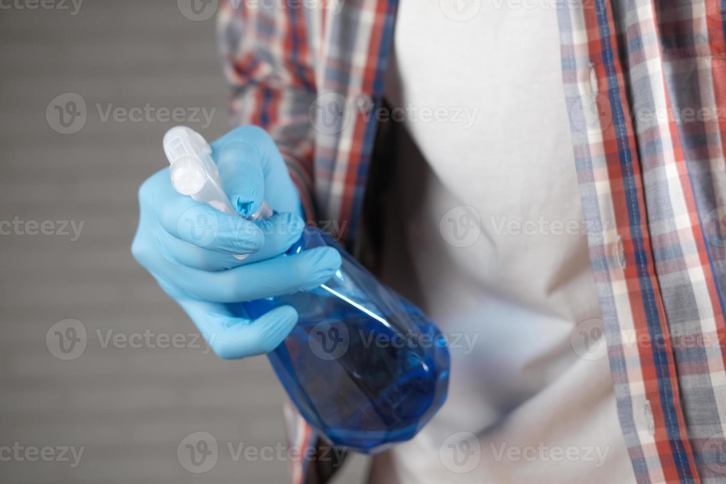 Hand in blauen Gummihandschuhen mit Sprühflaschen-Reinigungstisch foto