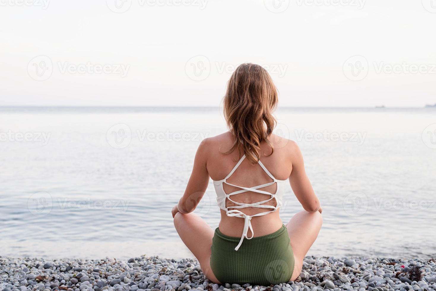Rückansicht einer jungen Frau, die am Strand meditiert foto