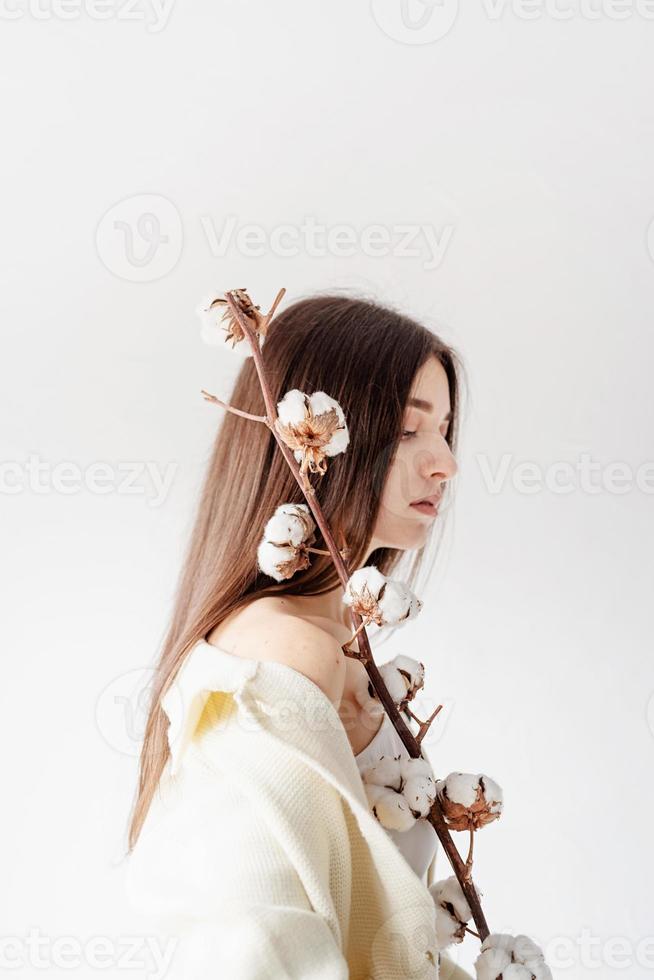 schöne Frau in gemütlicher Kleidung, die einen Zweig von Baumwollblumen hält foto