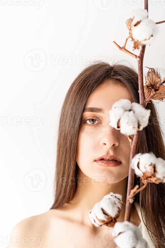 schöne Frau in gemütlicher Kleidung, die einen Zweig von Baumwollblumen hält foto