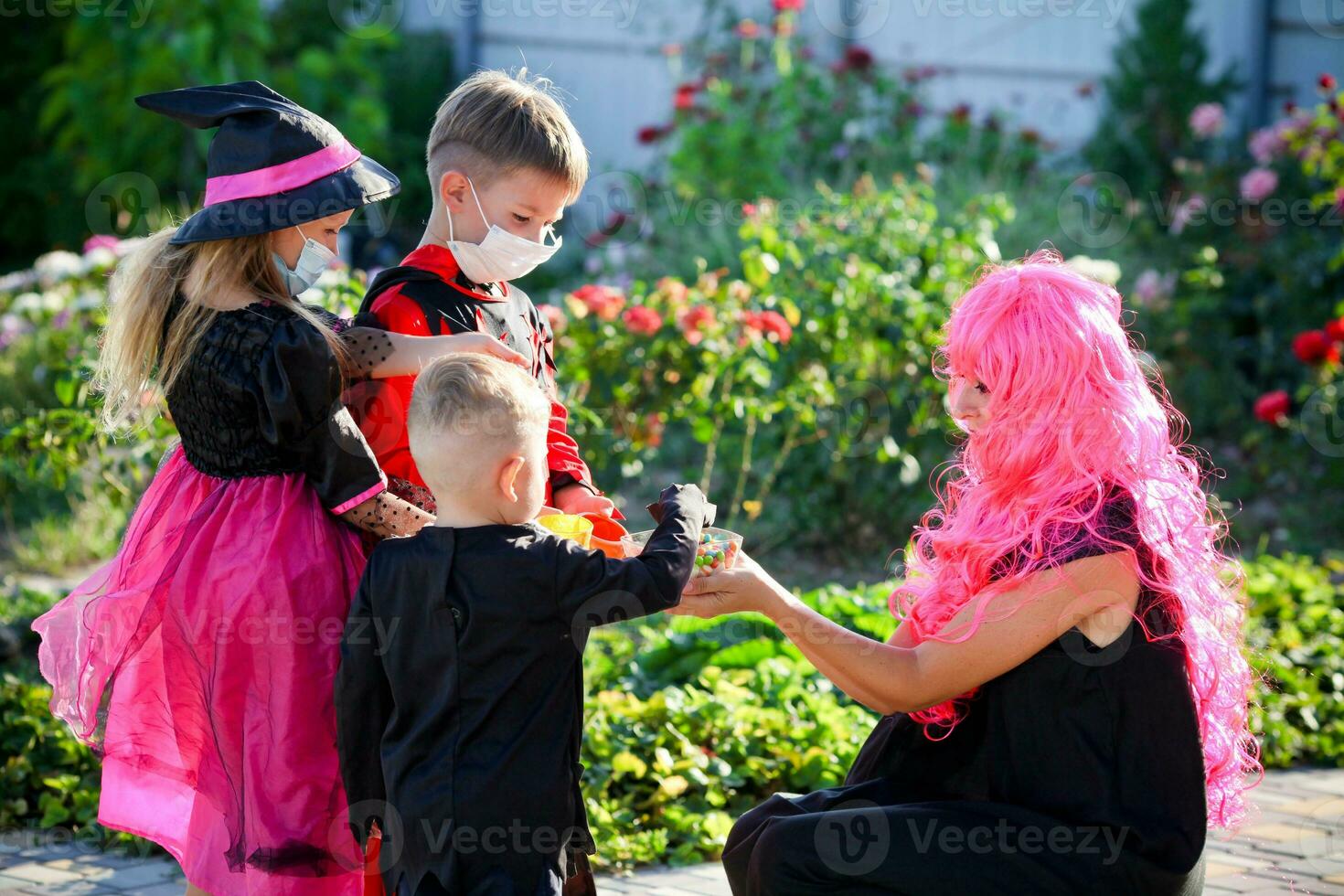 Kinder Trick oder behandeln im Halloween Kostüm und medizinisch Maske. ein Junge und ein Mädchen im Anzüge während das Coronavirus Pandemie erhalten Süßigkeiten von ein Frau . foto