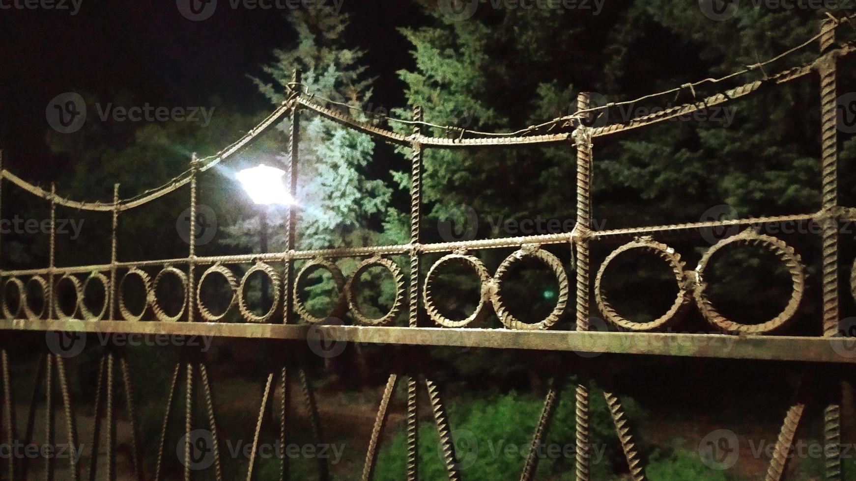 Metallzaun in der Nacht. künstliche Lichtstrahlen dringen durch foto