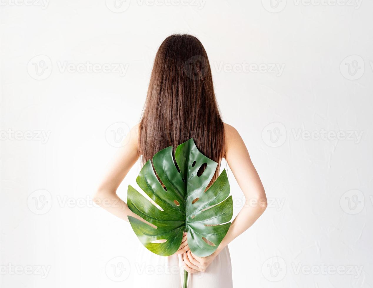 schöne Frau in gemütlichen Kleidern mit einem grünen Monstera-Blatt foto