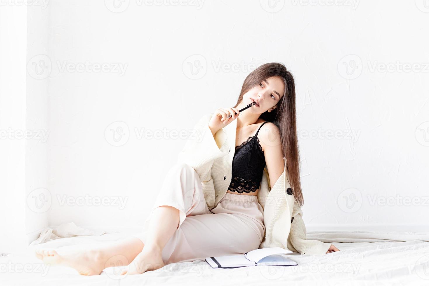 Frau in bequemer Hauskleidung, die auf dem Boden sitzt und Notizen schreibt foto