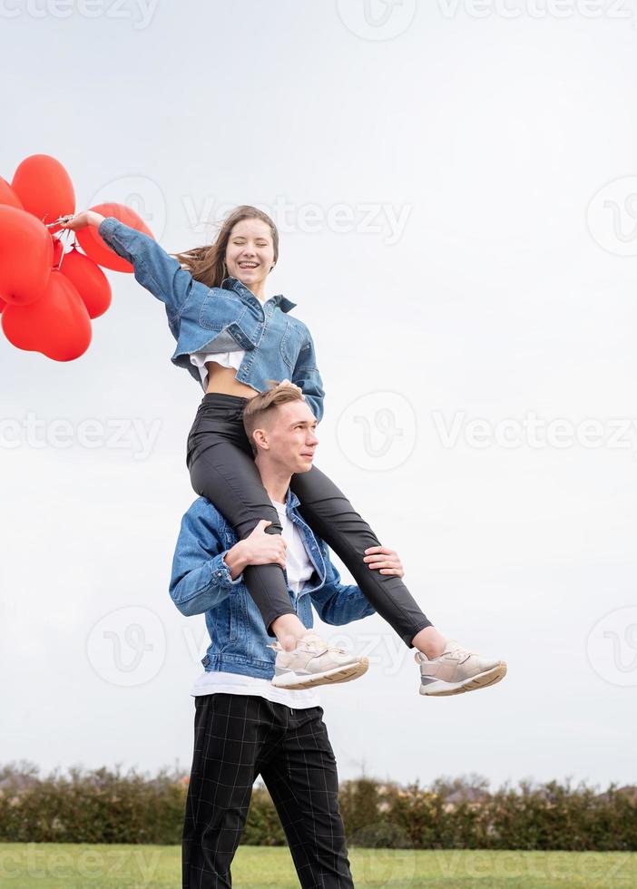 junges Liebespaar mit roten Luftballons, die sich im Freien umarmen und Spaß haben foto