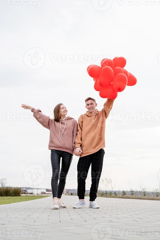 junges Liebespaar mit roten Luftballons, die sich im Freien umarmen und Spaß haben foto