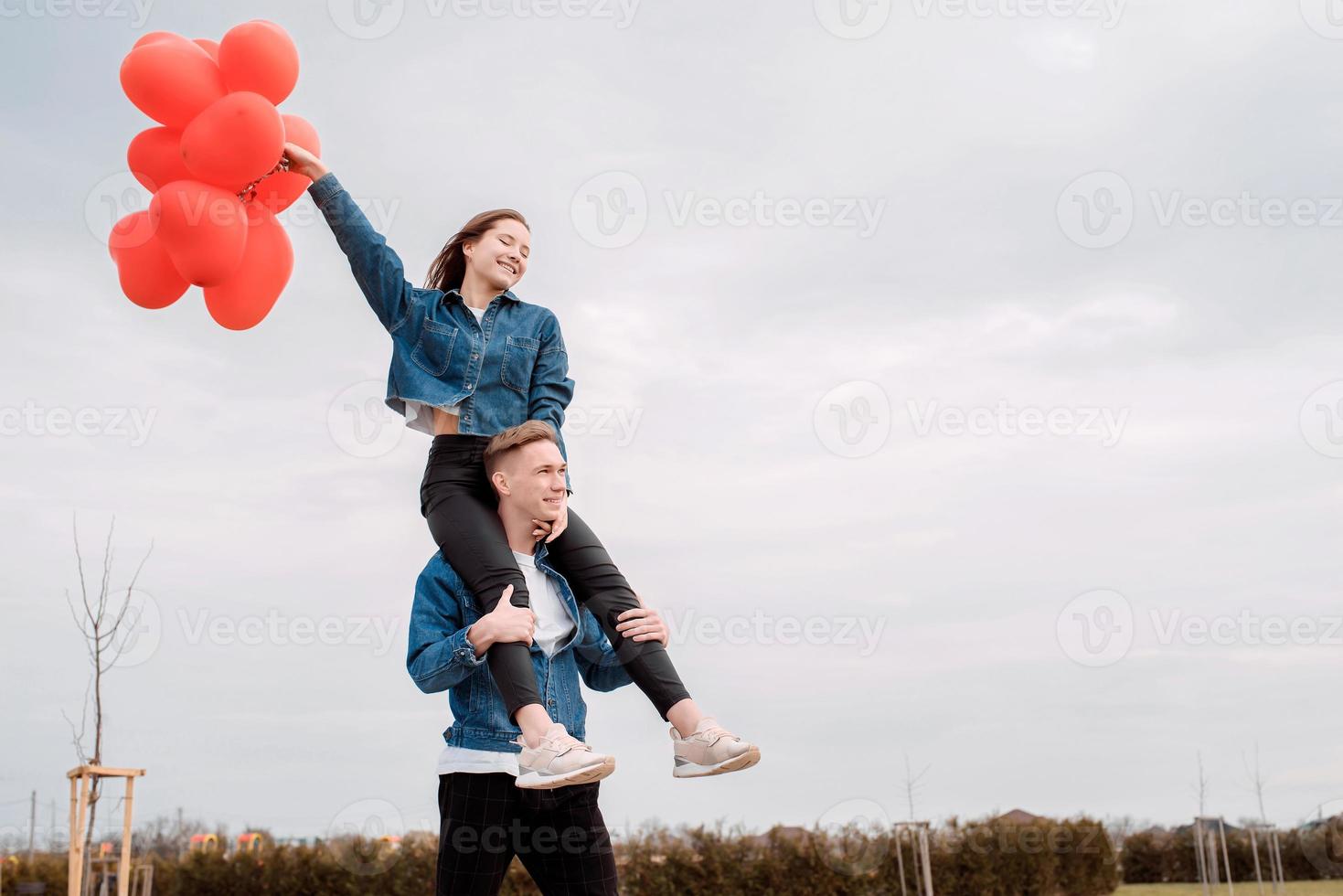 junges Liebespaar mit roten Luftballons, die sich im Freien umarmen und Spaß haben foto