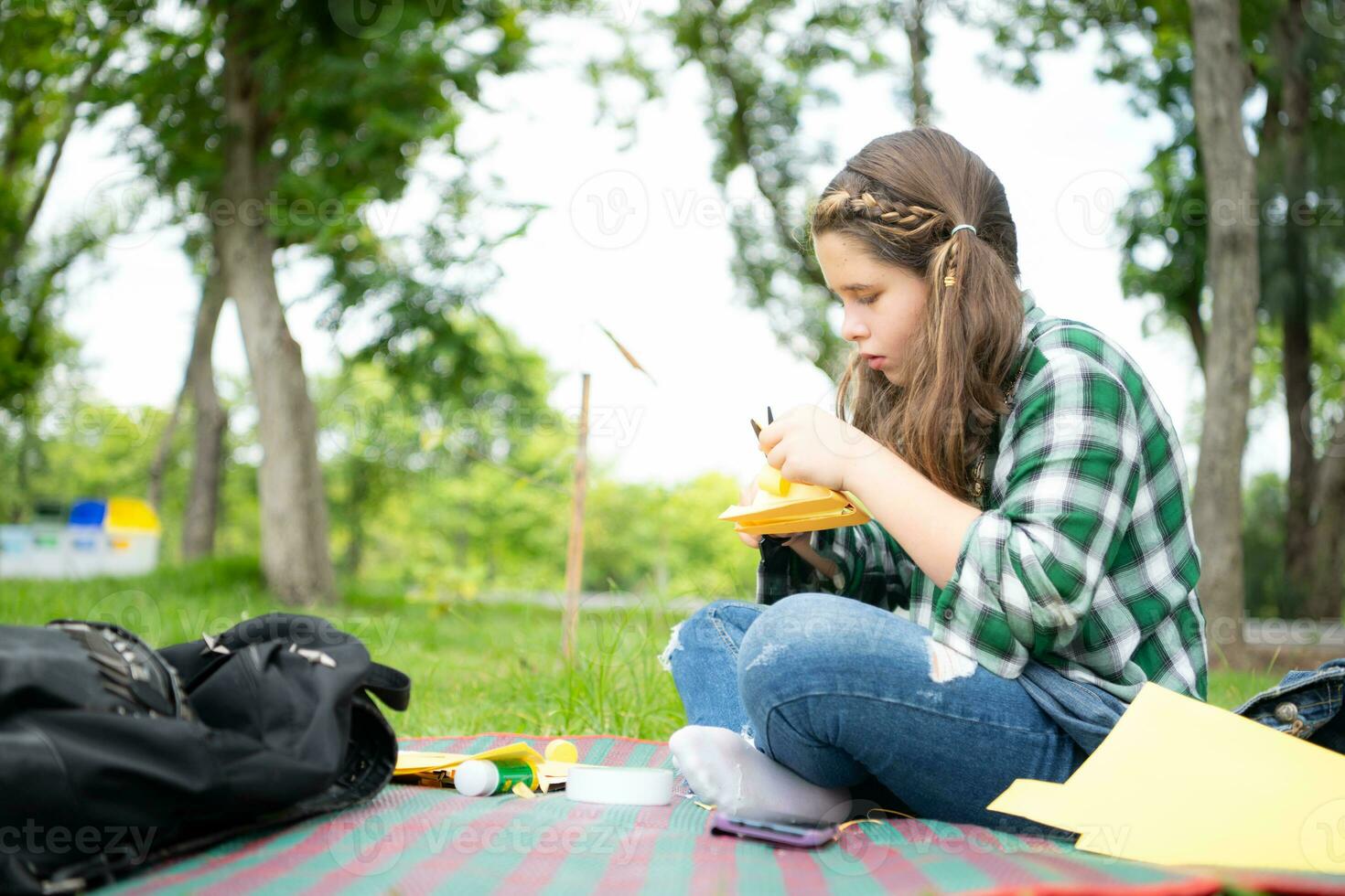 wenig Mädchen auf Ferien im das Park mit das Kunst von Herstellung ein Vogel Schnabel mit Papier können verwenden Ihre Finger zu Bewegung Ihre Mund. foto