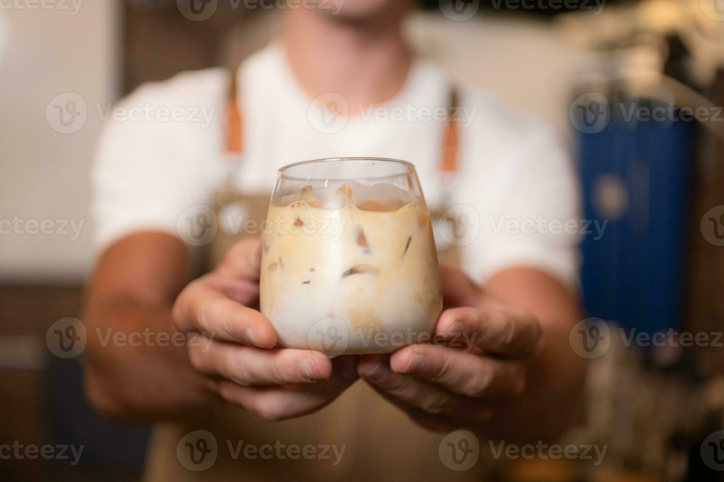 Barista halten ein Glas von kalt Latté Kaffee im seine Hände zu Kunde foto