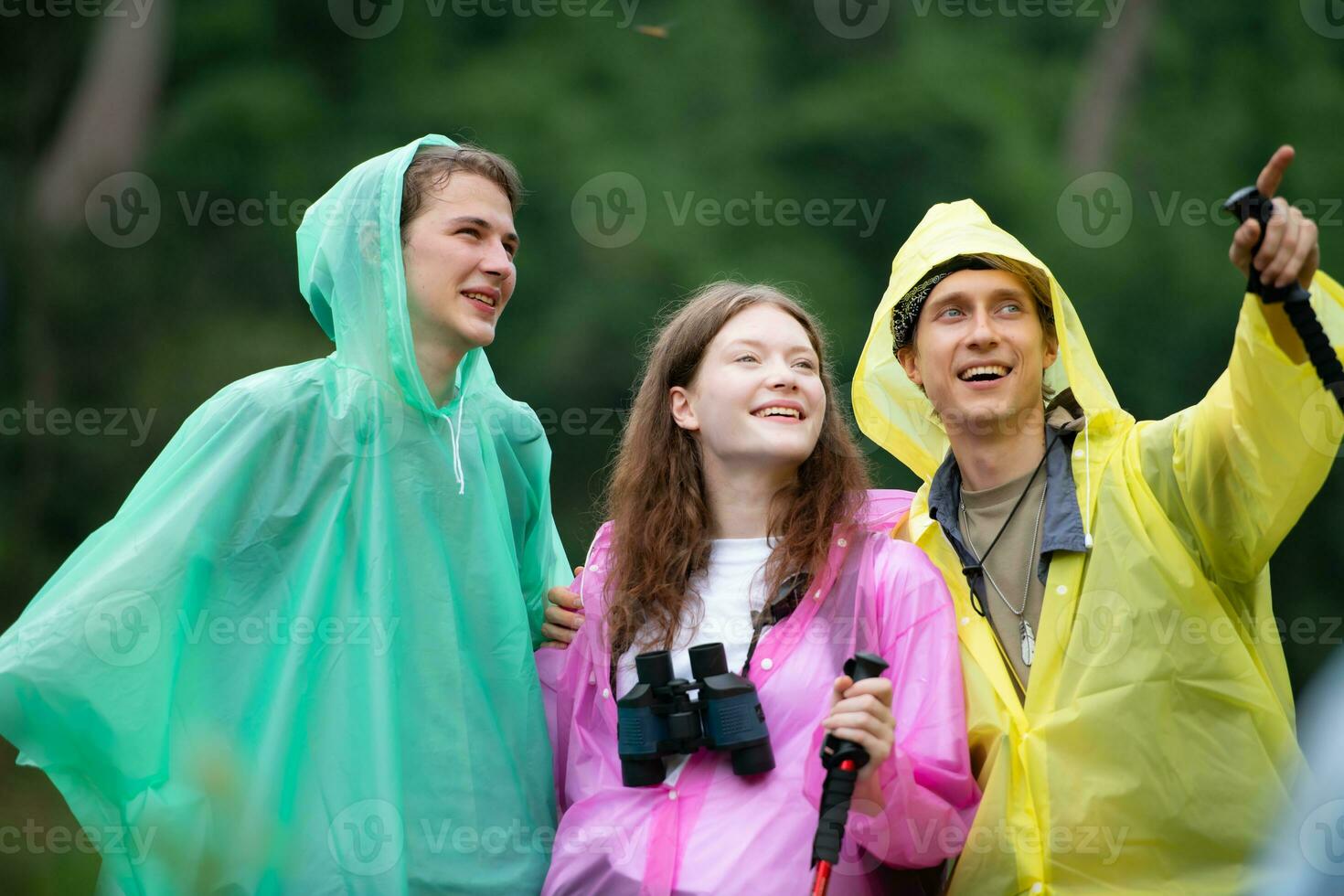 Gruppe von glücklich freunde im Regenmäntel und Regenmäntel suchen beim Berg und Wald nach das Regen gestoppt foto