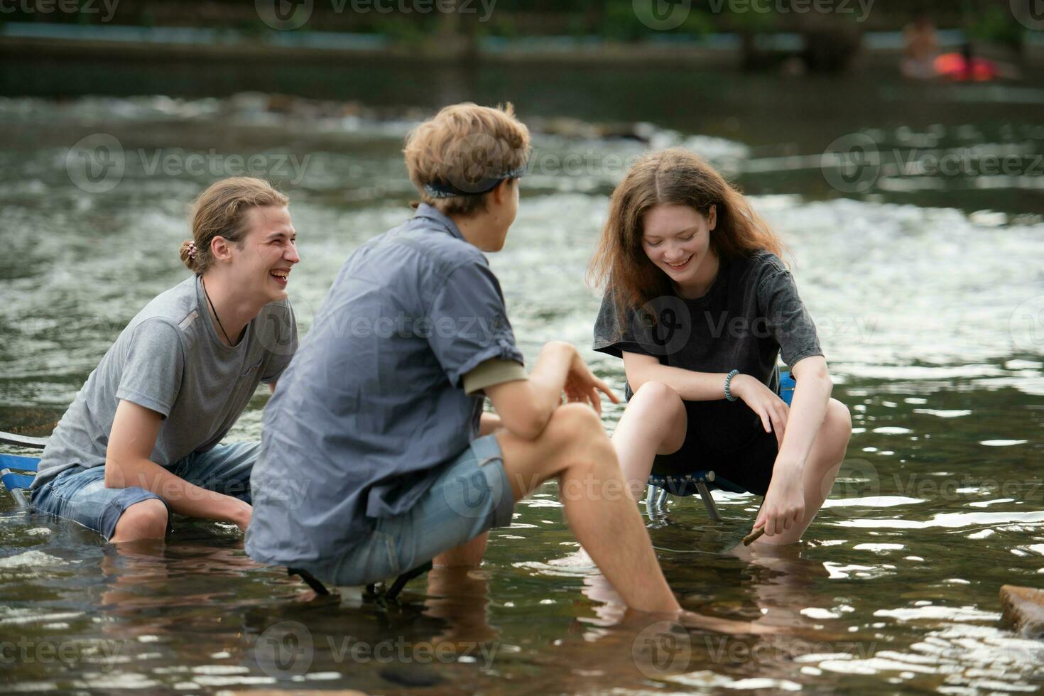 Gruppe von freunde sind reden und haben Spaß im das Mitte von das Fluss fließend im Vorderseite von das Campingplatz. foto