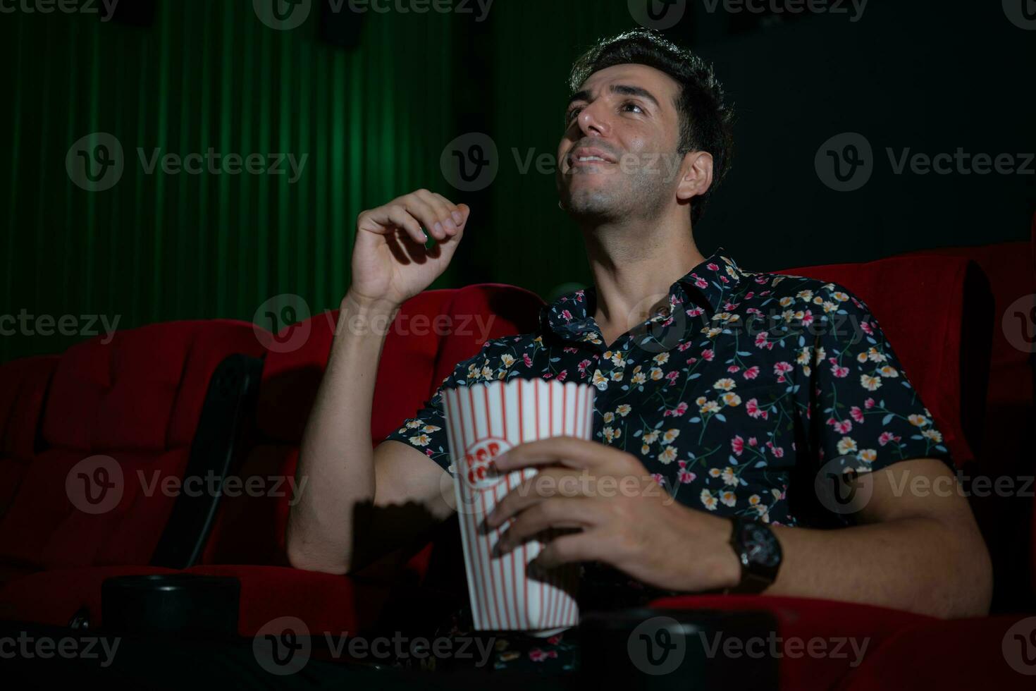 jung Mann Aufpassen Film und Essen Popcorn während Sitzung auf rot Couch foto