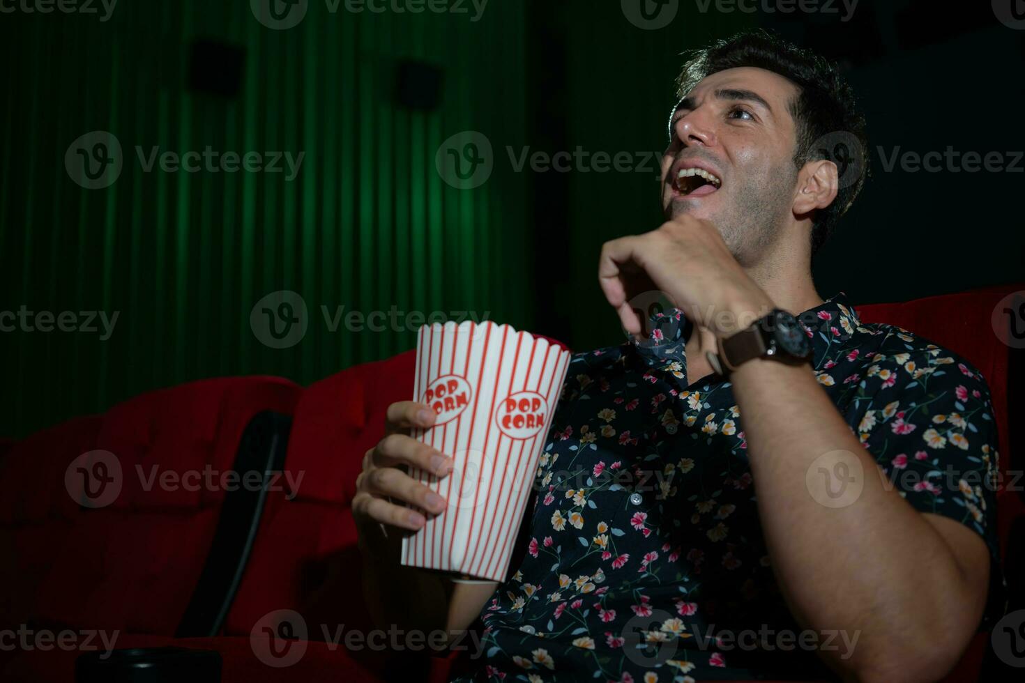 jung Mann Aufpassen Film und Essen Popcorn während Sitzung auf rot Couch foto