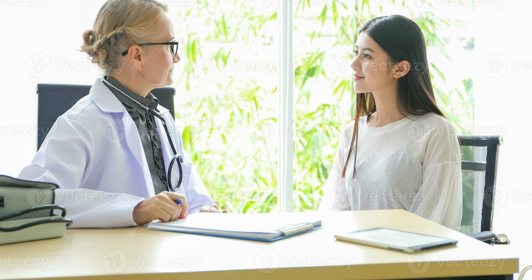 asiatisch Frau geduldig Sitzung mit Arzt Über ihr Krankheit und zeigen Röntgen Ergebnisse mit Blut Druck und Herz Bewertung Messung mit Stethoskop foto