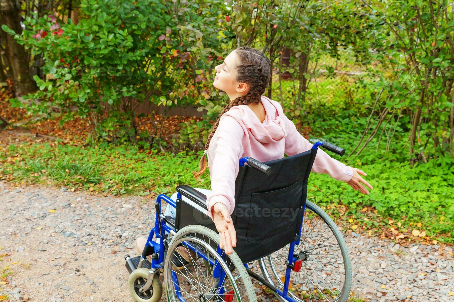 junge glückliche behinderte frau im rollstuhl unterwegs im krankenhauspark, der freiheit genießt. gelähmtes Mädchen im Rollstuhl für Behinderte im Freien in der Natur. Rehabilitationskonzept. foto