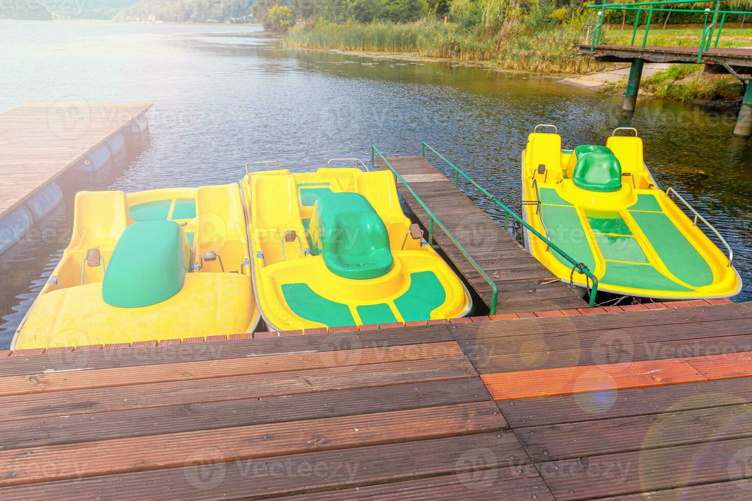 Tretboote oder Tretboote Katamarane Station. Gelbe Wasserfahrräder, die an sonnigen Sommertagen am Pier des Yachthafens am See gesperrt sind. Sommerfreizeitbeschäftigung im Freien. foto