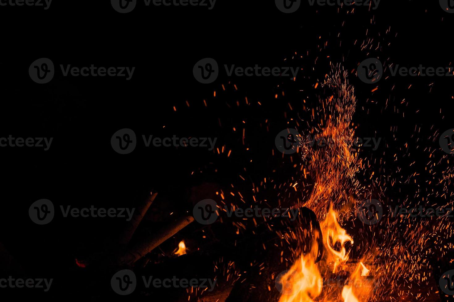 Funken prallen nachts von einem Lagerfeuer ab, nachdem ein Holzscheit hineingeworfen wurde foto