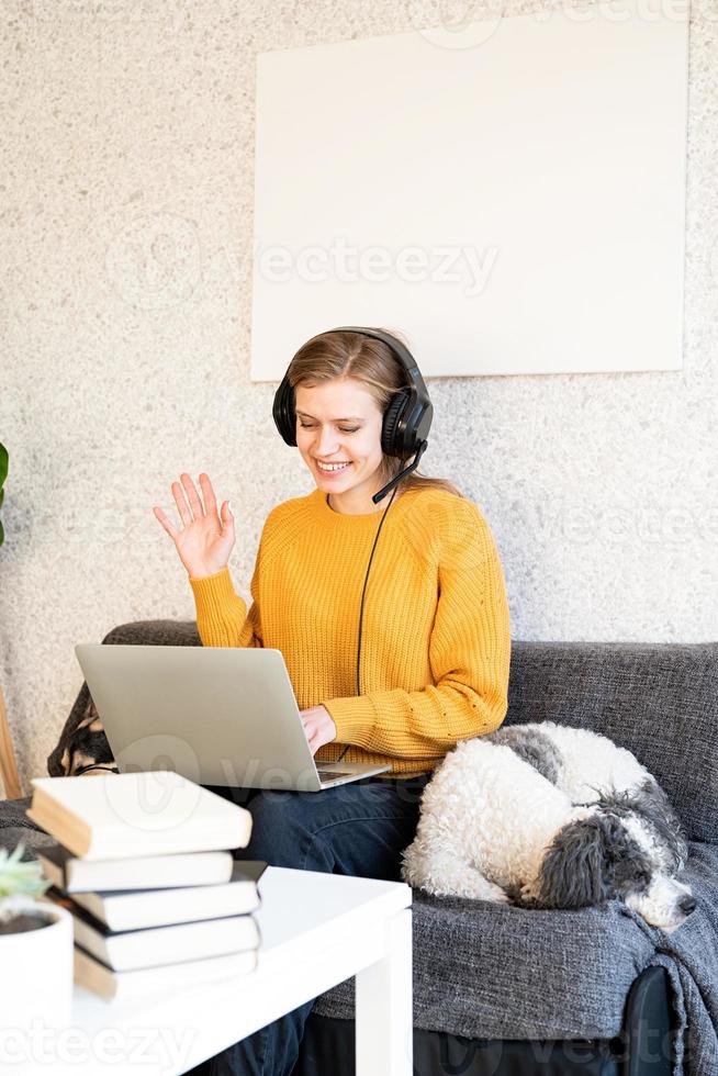 junge lächelnde Frau in schwarzen Kopfhörern, die online mit Laptop studiert? foto