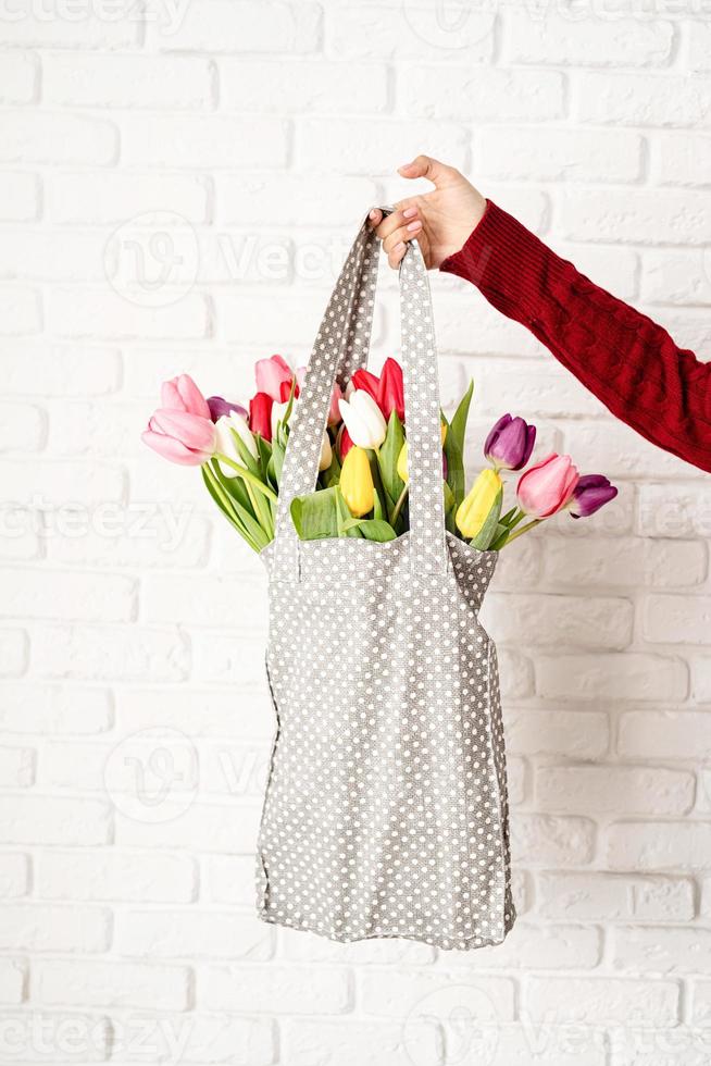 Frauenhand, die graue gepunktete Stofftasche mit bunten Tulpen hält foto