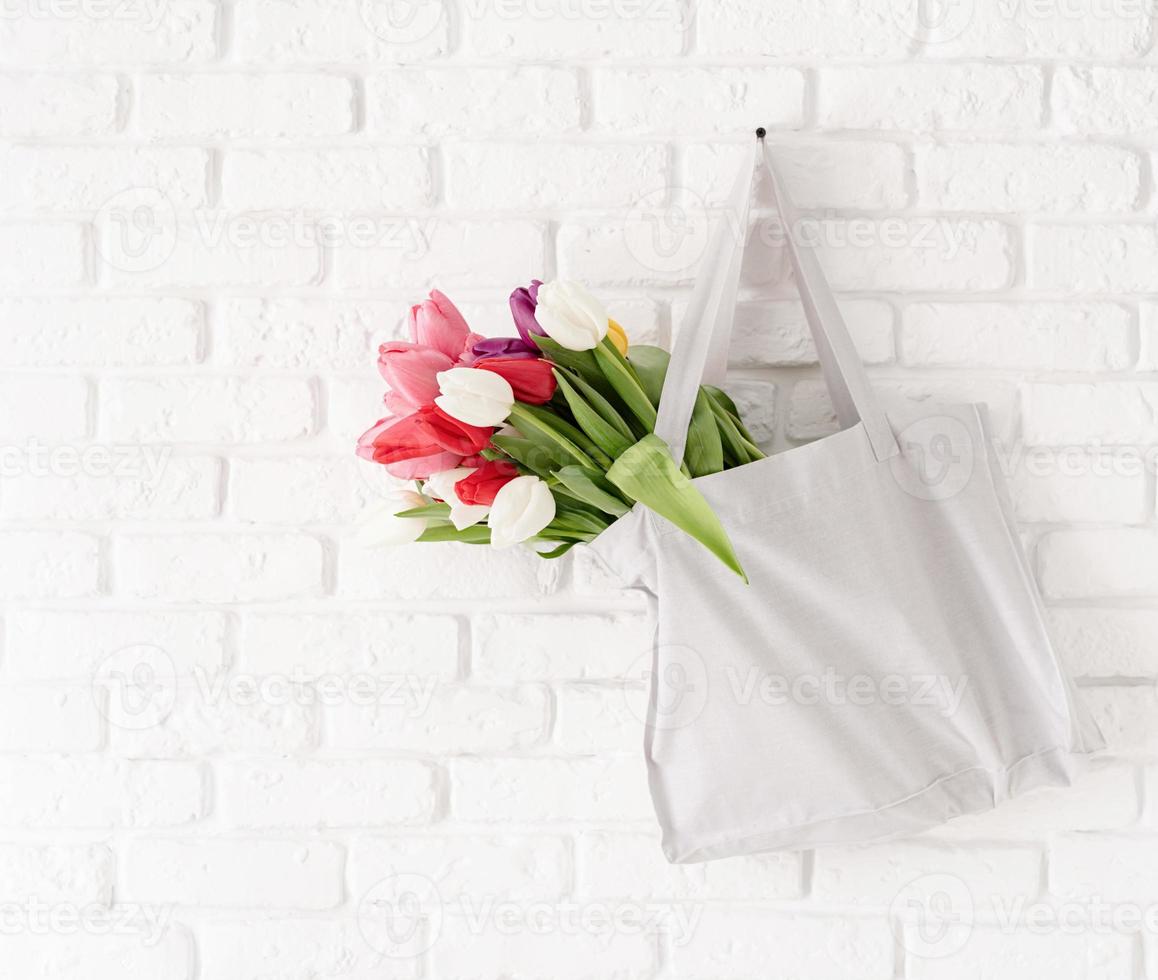 graue Stofftasche voller bunter Tulpen auf weißem Backsteinhintergrund foto