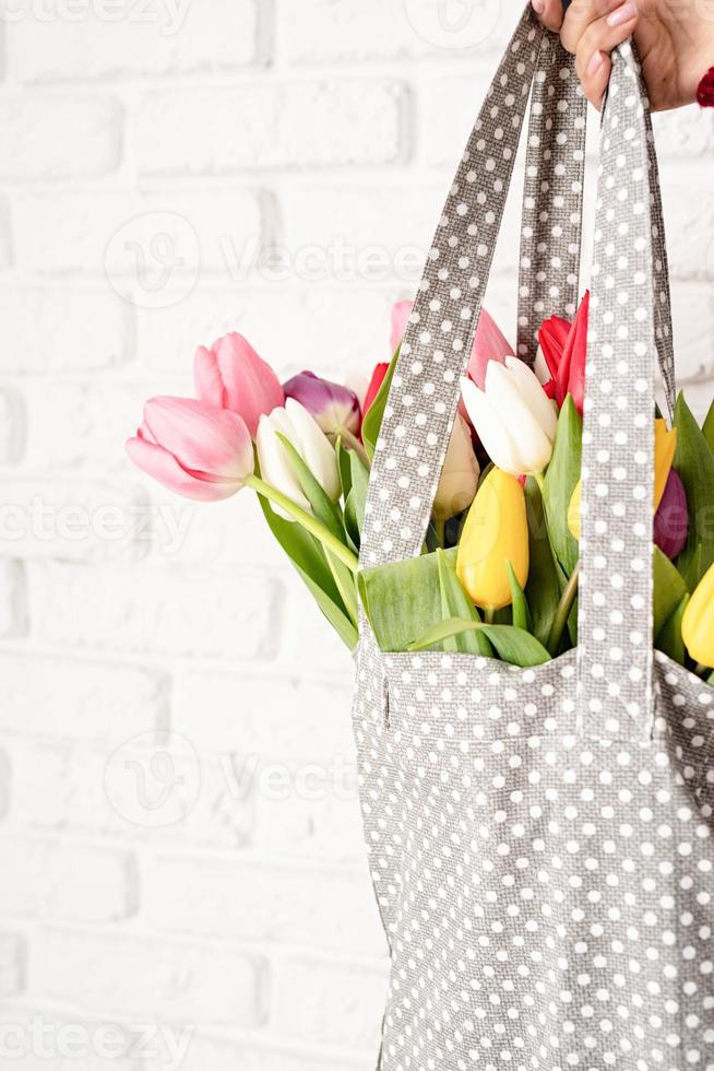 Frauenhand, die graue gepunktete Stofftasche mit bunten Tulpen hält foto