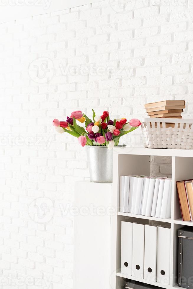 Eimer Tulpenblumen neben dem Bücherregal foto