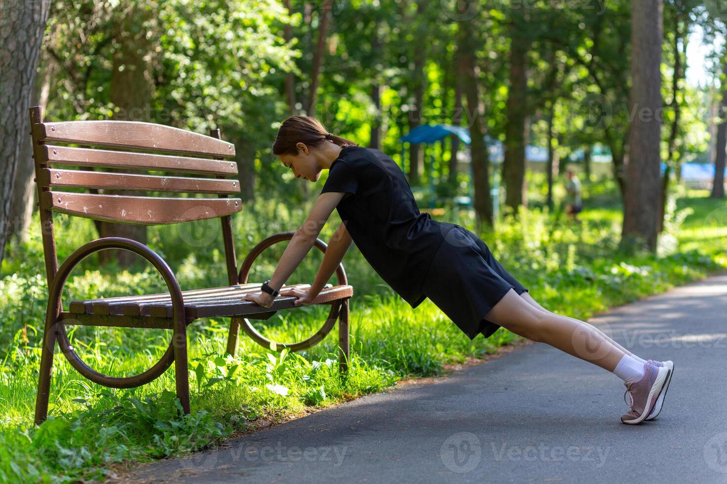 schön jung sportlich Frau im schwarz T-Shirt, schwarz kurze Hose und Rosa Sportschuhe Erwärmen oben ausüben Trizeps und Truhe foto