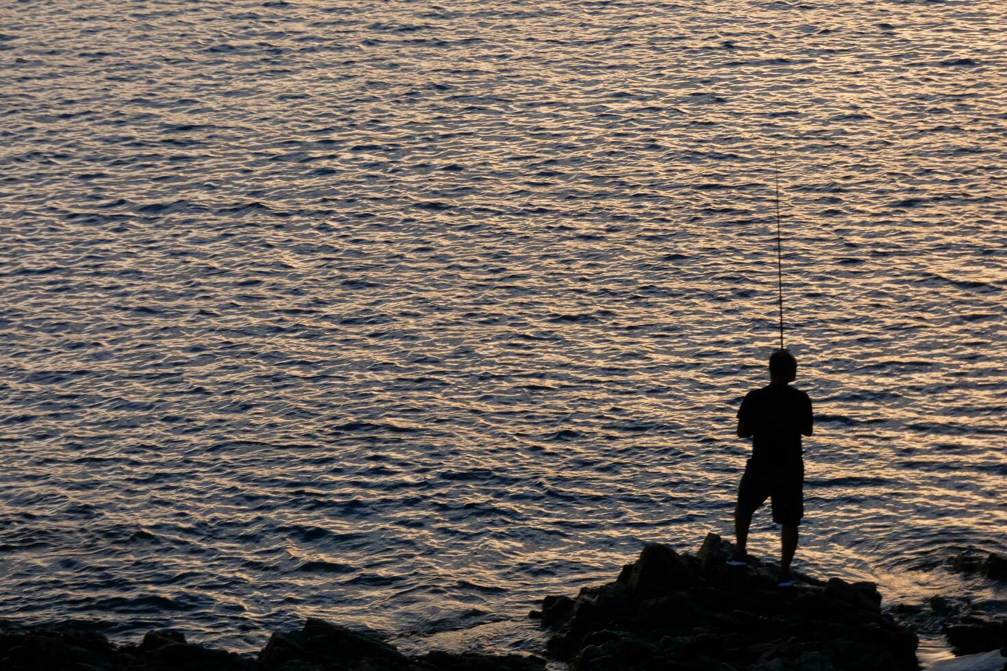 Mann von hinten beleuchtet mit ein Angeln Stange im das Meer foto