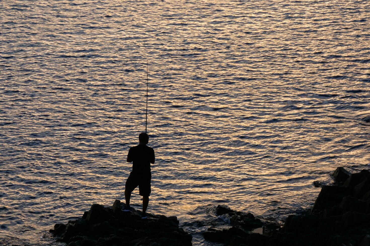 Mann von hinten beleuchtet mit ein Angeln Stange im das Meer foto