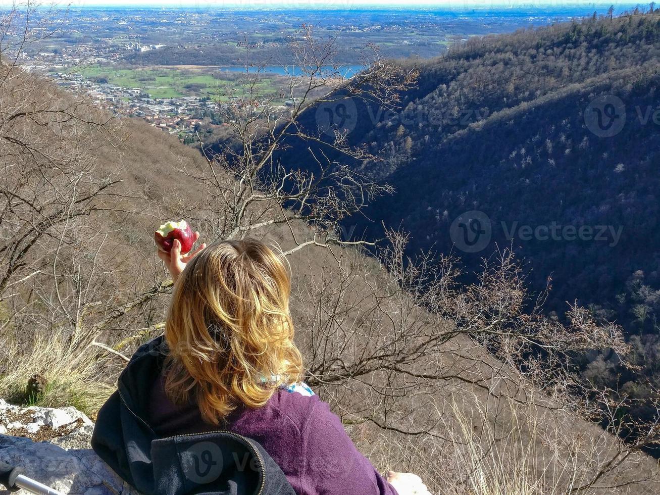 Frau mit blonden Haaren ruht sich aus und isst einen Apfel auf einem Berg foto